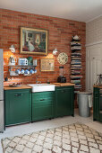 Kitchen cabinets with green fronts, with a shelf above and painting on the exposed brick wall