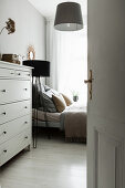 View past chest of drawers to bed and standard lamp in bedroom