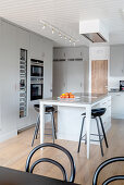 Grey built-in cupboards and central unit with bar stools in an open kitchen