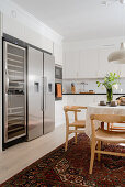 Wine cooler, fridge and freezer next to white fitted kitchen with dining area in the foreground