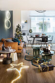 Weihnachtsgeschenke auf dem Teppich, leuchtender Stern, Ledersofa und Weihnachtsbaum in offenem Wohnraum