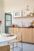 Küchenzeile mit Holzfront, darüber handglasierte Fliesen und Regal, Essbereich im Vordergrund