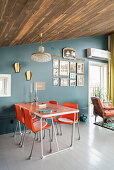 Orange dining set in front of blue-grey wall in open-plan interior with rustic wooden ceiling