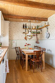 Dining table and chairs in country-house kitchen with wooden panelling and floral wallpaper
