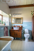 Freistehende Badewanne, antikes Waschtischmöbel und Toilette im Badezimmer mit hellblauen Wandfliesen