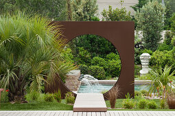 Pool with water spouts and moon gate in weathering steel panel in lush garden