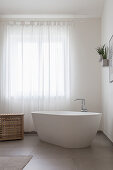 A freestanding bathtub in front of a curtained window in a bathroom