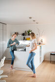 Two friends are standing at the kitchen counter in the open living room