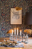 Kerzen und getrocknete Hortensienblüten in Glasflaschen auf rustikalem Holztisch