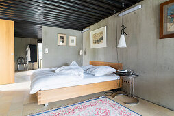 Doppelbett im Schlafzimmer mit Betonwänden, im Hintergrund Bad Ensuite
