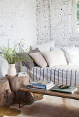 Sofa with cushions, coffee table and tree trunk stool in room with whitewashed brick wall