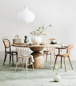 Various chairs around round wooden table with vase and asitatic place setting