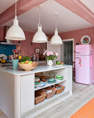Große Pendelleuchten im Industriestil und ein rosa Kühlschrank in einer hellen Küche mit Wänden in Rosatönen