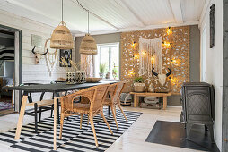 Dining table with rattan armchairs on black and white carpet, above boho hanging lights
