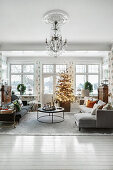 Illuminated Christmas tree in bright, open-plan living room with upholstered furniture