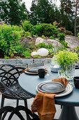 Gedeckter Gartentisch in Grau am sommerlichen Beet mit Natursteinmauer