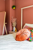 Round velvet cushion on bed in bedroom decorated in shades of terracotta