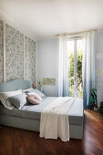 Bett und Holzvertäfelung mit Blumentapete in hellblauem Schlafzimmer