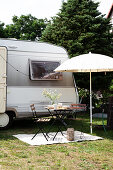 A table with two chairs and a sunshade in front of a caravan
