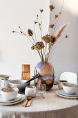 Gedeckter Tisch mit Leinendecke, Keramikgeschirr, Glasvase und Trockengräsern