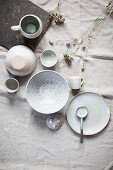 Keramikgeschirr und Trockengräser auf Tisch mit Leinendecke