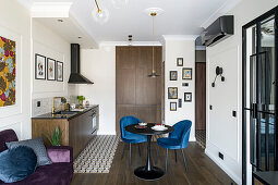 Dining area with blue upholstered chairs in front of small kitchen counter and purple sofa in open-plan interior