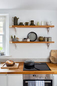 Küchenzeile mit Holzarbeitsplatte, darüber Regale in weißer Küche