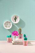 Cactus, carnation and faux painted stone cacti with sand in glasses below wall plates with cactus motifs