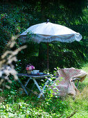Gartenstuhl mit geblümter Decke und Tisch unter Sonnenschirm