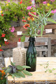 Zinnias with bentgrass, woodoats, sage and branch of berries in vintage swing-top bottle