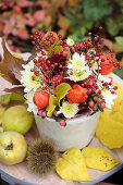 Autumn arrangement with lantern flowers, chrysanthemums, rose hips and hypericum, next to quinces