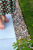Women's feet on concrete paving next to gravel bed in garden