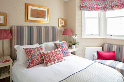 Double bed with cushions and tall upholstered headboard, pictures in gold frames on a wallpapered wall