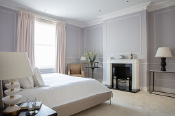 Double bed and fireplace in bedroom with light grey walls