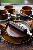 Chocolate éclair on ceramic plate with brown cups in the background