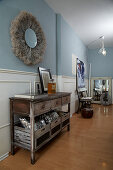 Old sideboard, above it boho mirror on light blue wall