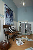 Vintage bench, above it modern art in the room with blue walls with white wainscoting, drawings scattered on the floor