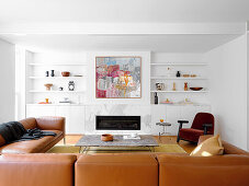 Brown leather sofa in white living room with shelves and modern art above the fireplace