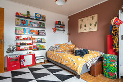 A bed, shelves of colourful books and a play kitchen in a children's room