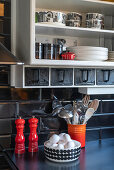 Kitchen utensils against black wall tiles on a black work surface
