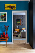 Bunte Kunstwerke an Wand mit blauer Tapete, Blick ins Schlafzimmer
