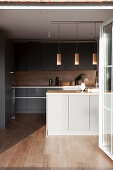 Dark fitted kitchen cabinet fronts, light kitchen counter in the foreground, with pendant lights hanging above it