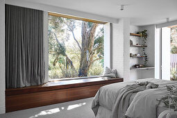 Double bed in the bedroom with white painted brick walls, built-in wooden bench in front of panorama window