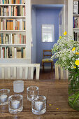 Tea lights and bouquet of flowers on old wooden table, bookshelf and hallway in background