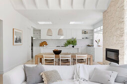 Open living room with bright sofa, fireplace, dining area, and white fitted kitchen cabinets