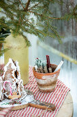 Gingerbread house, candles in terracotta pot and vase with coniferous branches