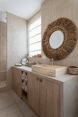 Gefliestes Badezimmer in Beigetönen, runder Spiegel mit Bastrahmen