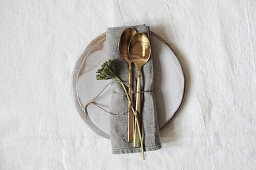 Place setting with linen napkin, golden cutlery and wild flower