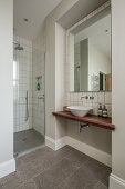 Waschtisch, darüber großformatiger Spiegel und Duschkabine im Bad mit weißen Wandfliesen