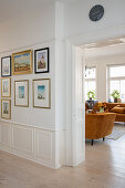 Blick vom Flur mit Bildersammlung ins Wohnzimmer auf braun-orangefarbenes Plüschsofa